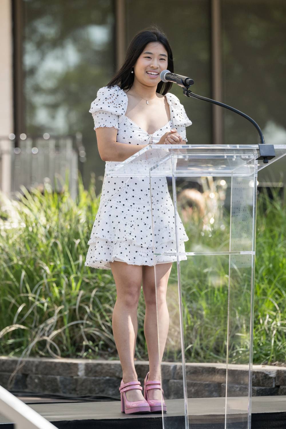 A person in a white polka dot dress speaking at a podium.